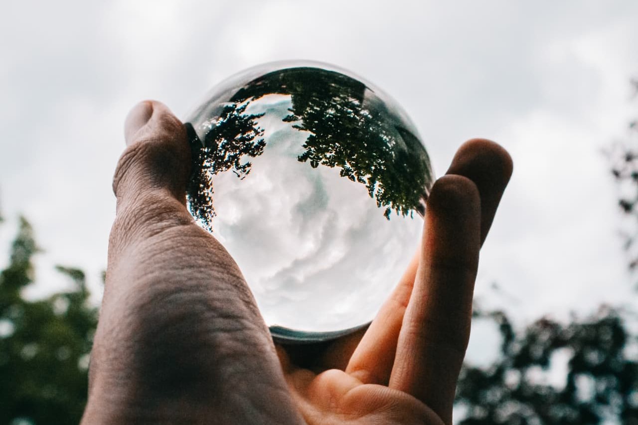 A hand holding a glass ball that turns the trees and clouds behind it upside down inside the sphere